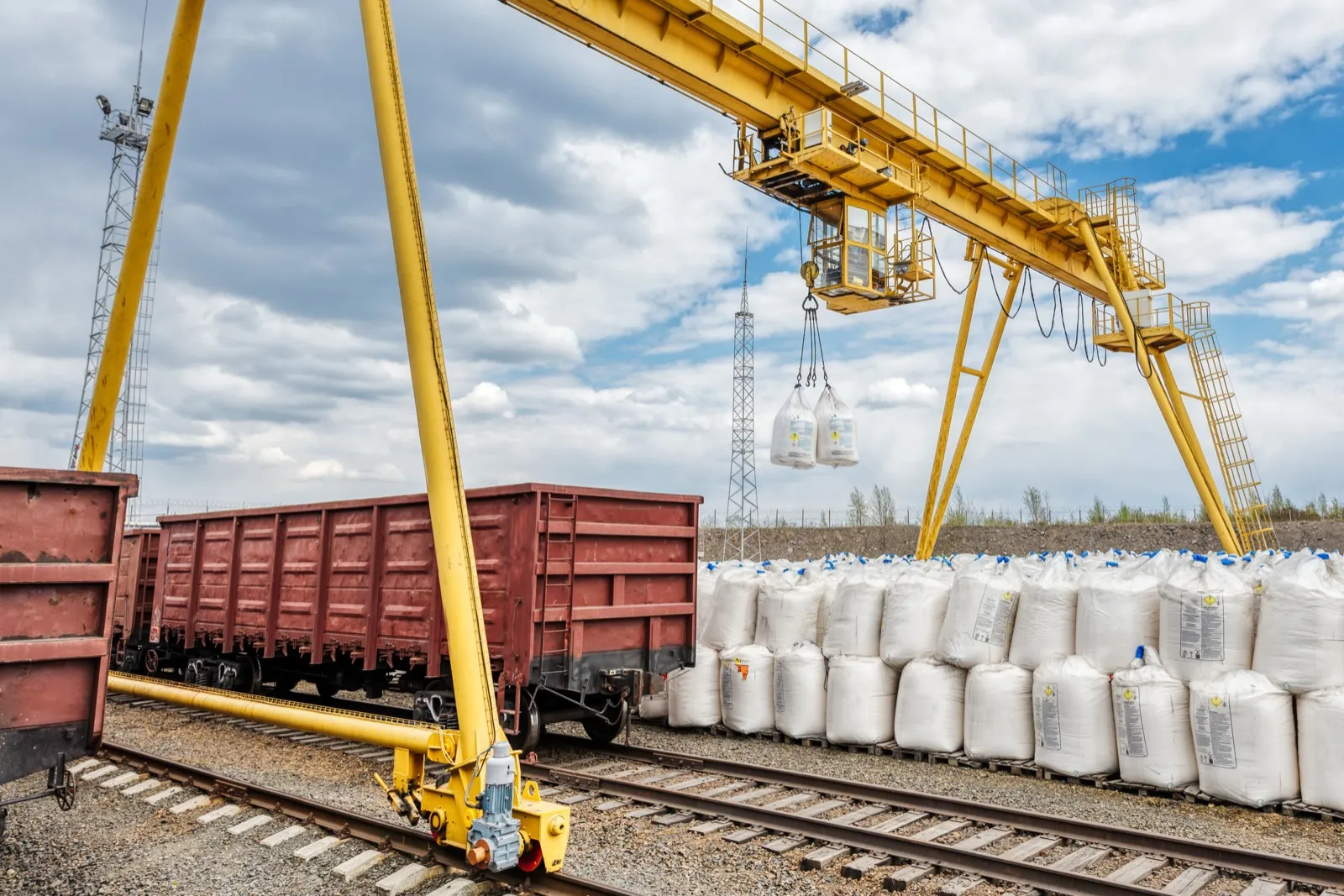 Outdoor rail-mounted gantry crane lifting bulk material bags over rail cars